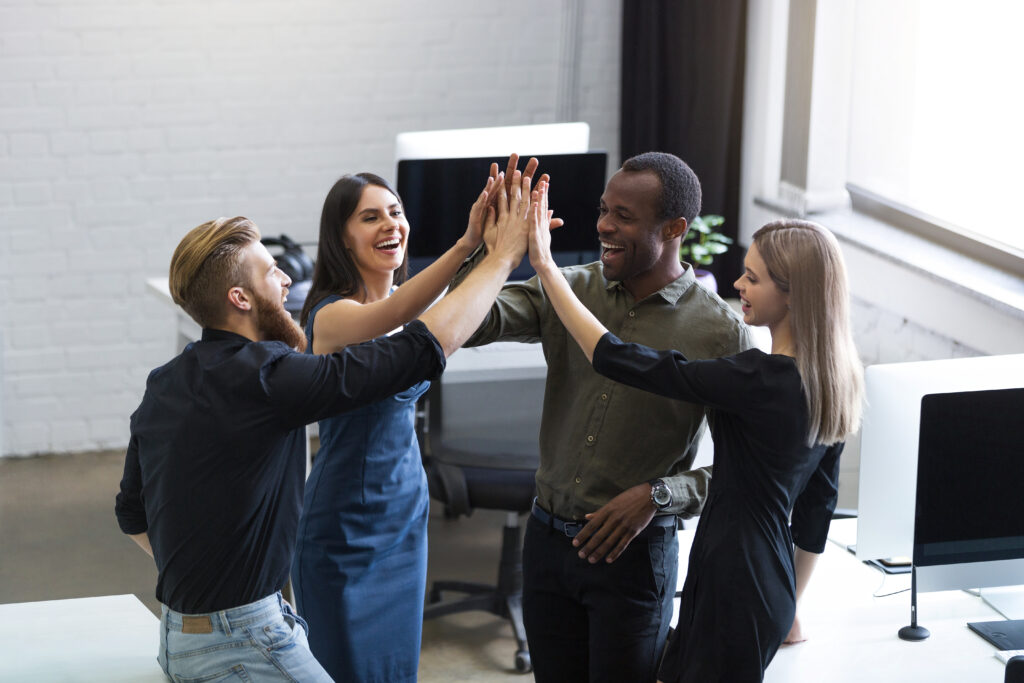 Grupo de jovens colegas dando um high five uns aos outros enquanto estão em um escritório